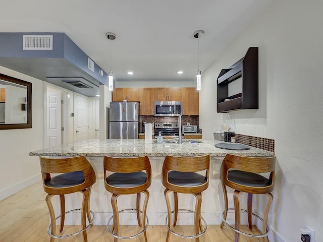 kitchen with stainless steel appliances, light stone countertops, light hardwood / wood-style floors, decorative backsplash, and pendant lighting