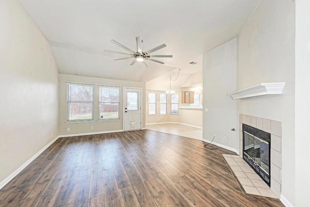 unfurnished living room with a tile fireplace, vaulted ceiling, wood-type flooring, and ceiling fan with notable chandelier