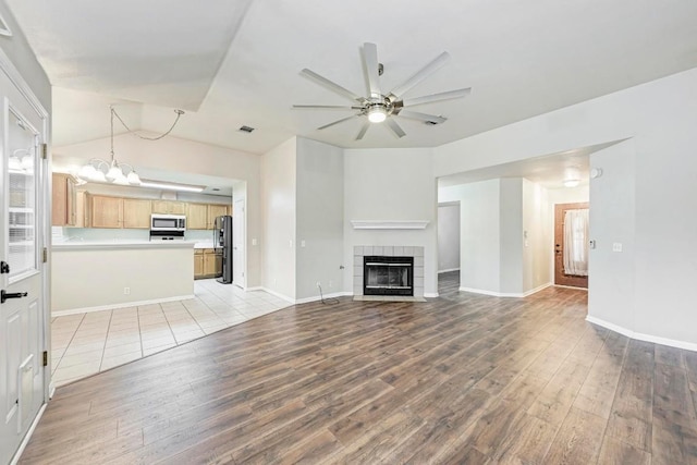 unfurnished living room featuring ceiling fan with notable chandelier, lofted ceiling, light hardwood / wood-style floors, and a tile fireplace