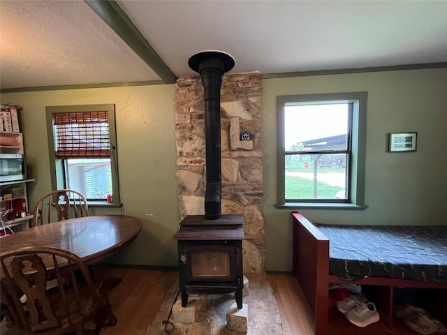 interior space featuring ornamental molding, wood-type flooring, beam ceiling, and a wood stove