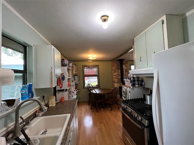 kitchen with sink, stainless steel gas range, white fridge, white cabinets, and light wood-type flooring