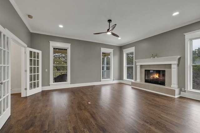 unfurnished living room with a tiled fireplace, ornamental molding, dark wood-type flooring, and ceiling fan