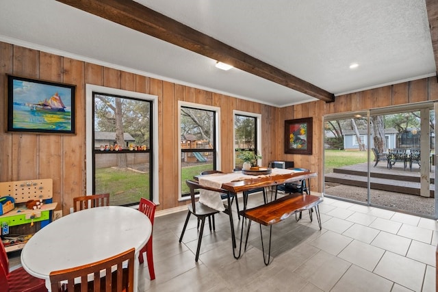 dining space featuring wooden walls, beam ceiling, a textured ceiling, and a wealth of natural light