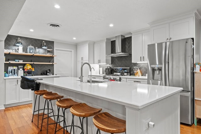 kitchen with stainless steel appliances, a kitchen island with sink, white cabinets, and wall chimney exhaust hood