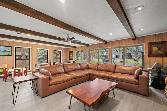 living room featuring beamed ceiling, a healthy amount of sunlight, a textured ceiling, and wood walls