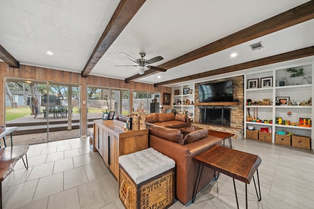 living room featuring built in shelves, wood walls, a textured ceiling, beamed ceiling, and a fireplace