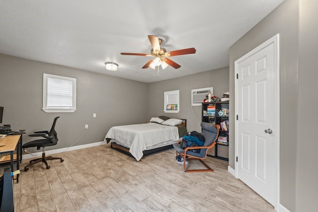 bedroom with a wall mounted air conditioner, ceiling fan, and light wood-type flooring