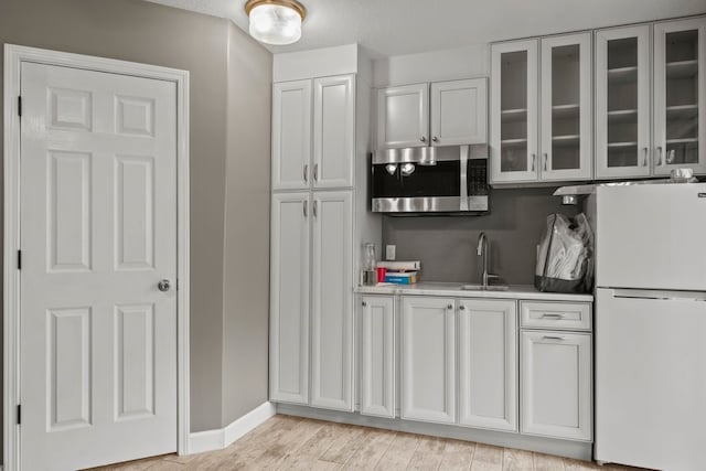 kitchen featuring white refrigerator, sink, light hardwood / wood-style flooring, and white cabinets