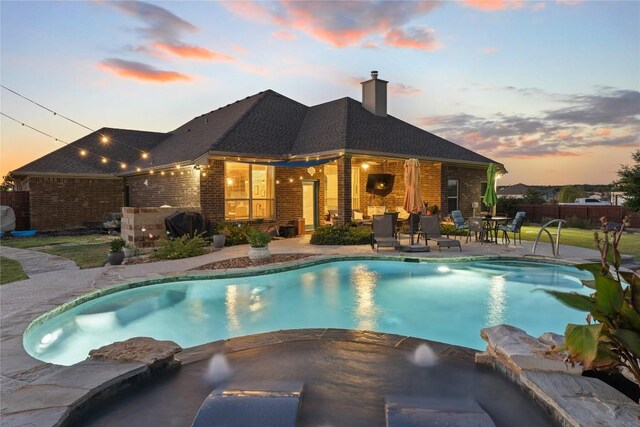 pool at dusk featuring a patio, a pool with connected hot tub, and fence