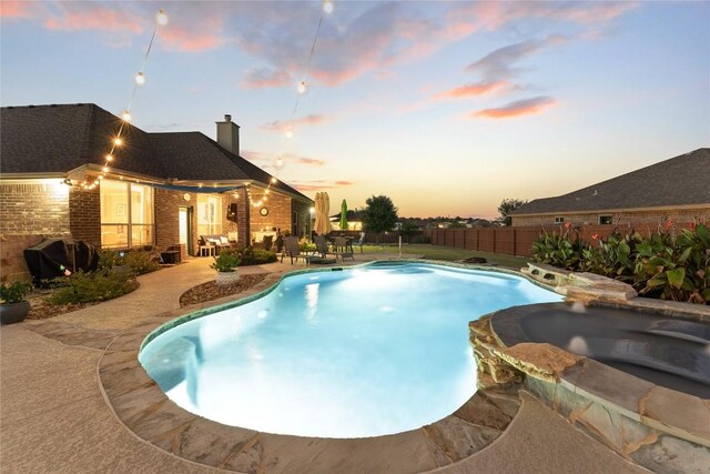 view of swimming pool with grilling area, fence, a pool with connected hot tub, and a patio area