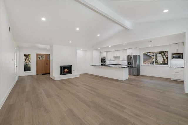 unfurnished living room featuring vaulted ceiling with beams, a large fireplace, light hardwood / wood-style floors, and a wealth of natural light