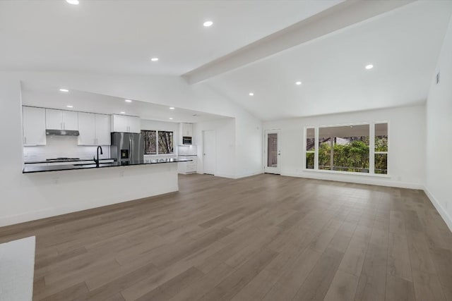 unfurnished living room with light wood-type flooring, sink, and lofted ceiling with beams