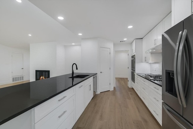 kitchen with sink, white cabinetry, stainless steel appliances, a large fireplace, and light wood-type flooring