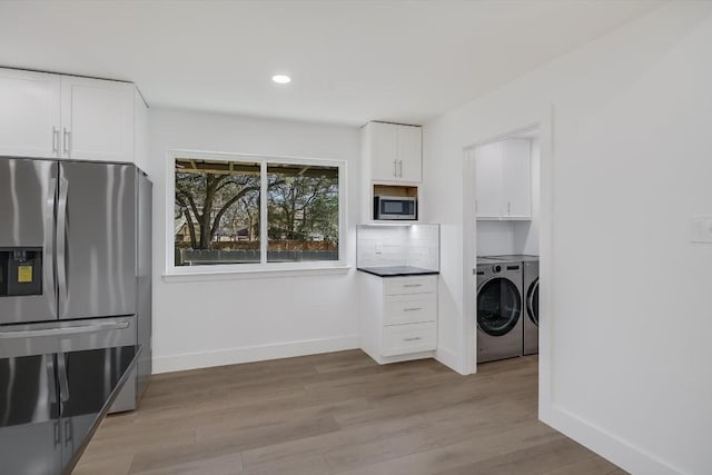 kitchen with washing machine and clothes dryer, white cabinetry, appliances with stainless steel finishes, light hardwood / wood-style floors, and decorative backsplash