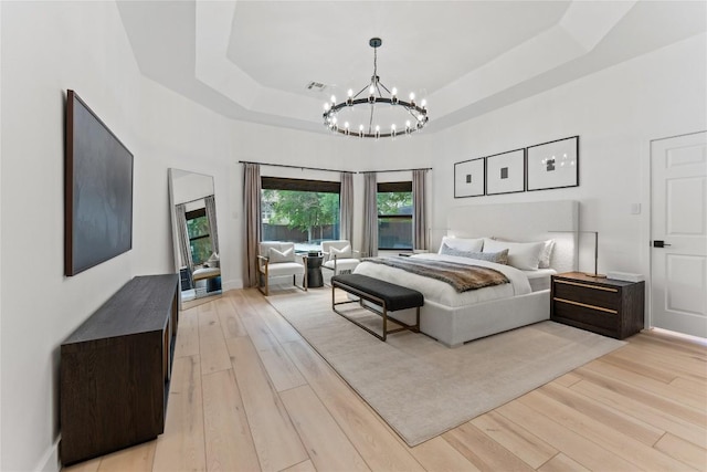 bedroom featuring a towering ceiling, light wood finished floors, a tray ceiling, and a notable chandelier