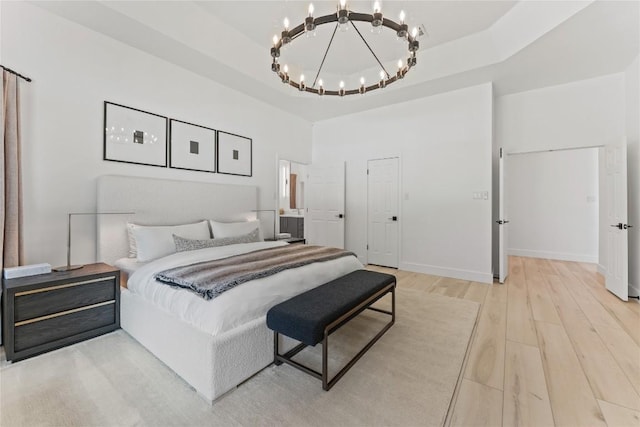 bedroom featuring a raised ceiling, baseboards, a notable chandelier, and light wood finished floors