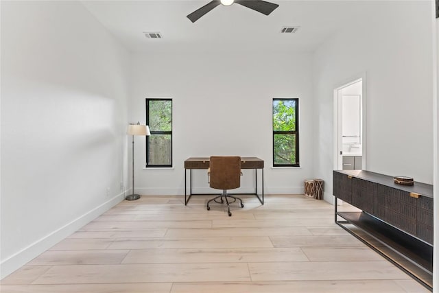 home office featuring light wood-style floors, visible vents, baseboards, and a ceiling fan