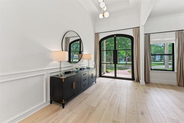 doorway to outside with light wood-style flooring, ornamental molding, a decorative wall, and wainscoting