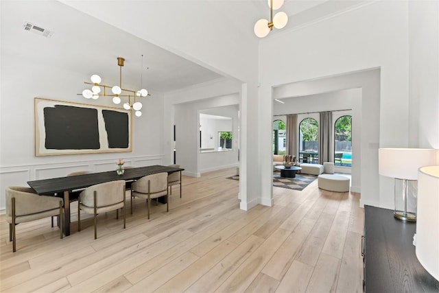 dining area featuring light wood finished floors, visible vents, crown molding, a decorative wall, and a notable chandelier