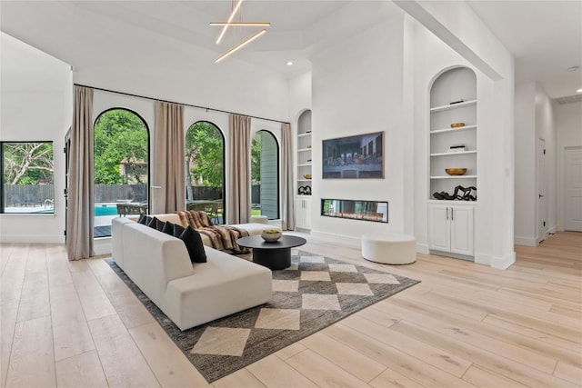 living area with built in shelves, a glass covered fireplace, light wood-style floors, and baseboards