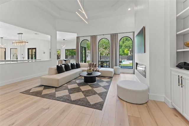 living room featuring baseboards, light wood-type flooring, a towering ceiling, and a notable chandelier