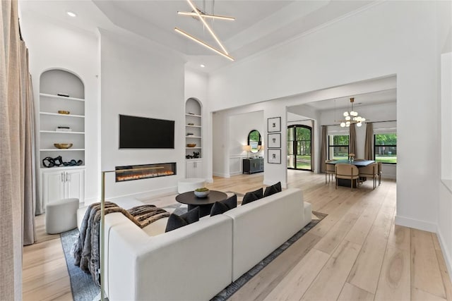 living room featuring built in features, a glass covered fireplace, a chandelier, light wood-type flooring, and baseboards