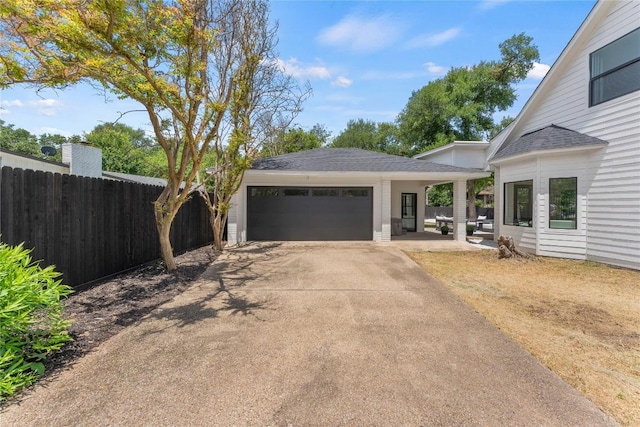 view of front facade with an outbuilding, roof with shingles, an attached garage, fence, and driveway