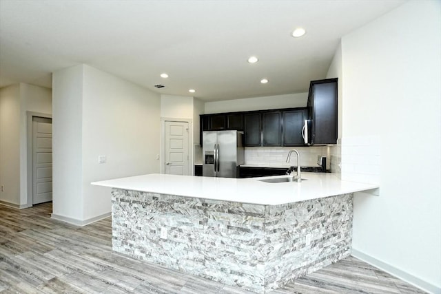 kitchen with tasteful backsplash, stainless steel fridge, kitchen peninsula, and sink