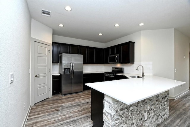 kitchen with appliances with stainless steel finishes, sink, hardwood / wood-style floors, and kitchen peninsula