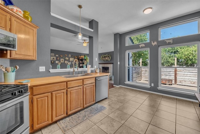 kitchen with sink, light tile patterned floors, appliances with stainless steel finishes, hanging light fixtures, and a brick fireplace