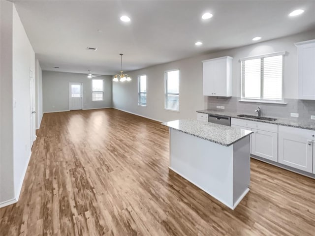 kitchen featuring a center island, stainless steel dishwasher, white cabinets, and light stone counters