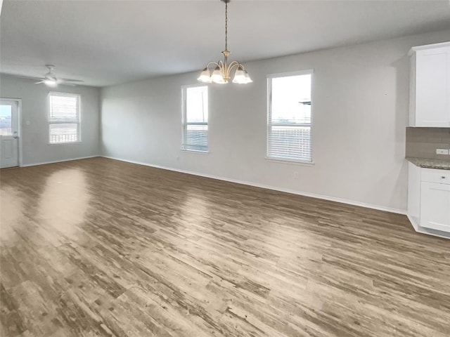 unfurnished dining area featuring ceiling fan with notable chandelier and hardwood / wood-style floors