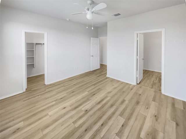 unfurnished bedroom with a spacious closet, a closet, ceiling fan, and light wood-type flooring