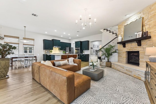 living room featuring a stone fireplace, hardwood / wood-style floors, and a notable chandelier