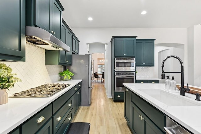 kitchen with stainless steel appliances, sink, light wood-type flooring, and decorative backsplash