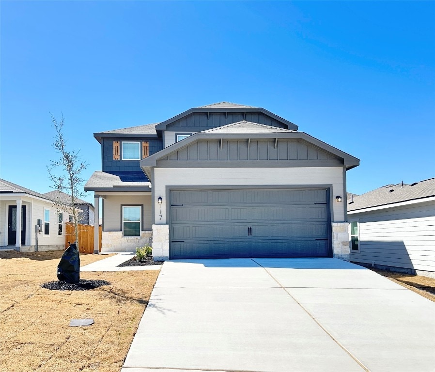 view of front of house featuring driveway, stone siding, a garage, and board and batten siding