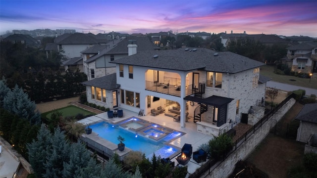 back house at dusk with a swimming pool with hot tub, a balcony, an outdoor hangout area, and a patio area