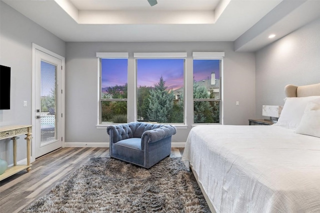 bedroom featuring access to exterior, hardwood / wood-style floors, and a raised ceiling