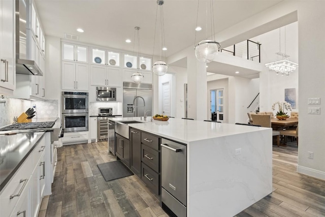 kitchen featuring pendant lighting, tasteful backsplash, white cabinetry, built in appliances, and a center island with sink