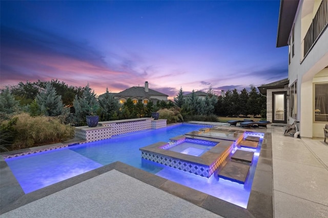 pool at dusk with an in ground hot tub and a patio