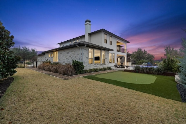 back house at dusk featuring a balcony and a yard