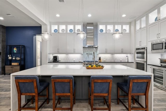 kitchen featuring appliances with stainless steel finishes, a kitchen breakfast bar, wall chimney range hood, a large island, and white cabinets