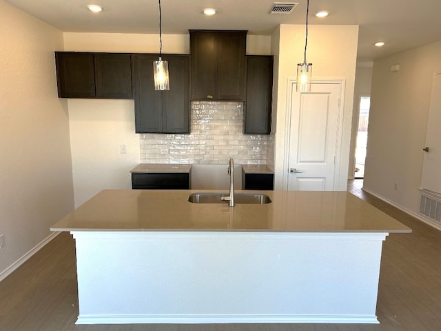 kitchen with visible vents, dark wood-type flooring, a sink, a kitchen island with sink, and backsplash