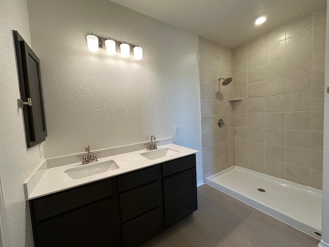 bathroom with double vanity, a tile shower, a sink, and a textured wall