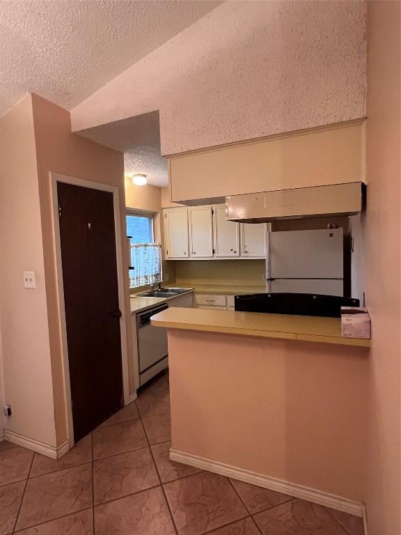 kitchen with a textured ceiling, dishwasher, kitchen peninsula, white fridge, and white cabinets