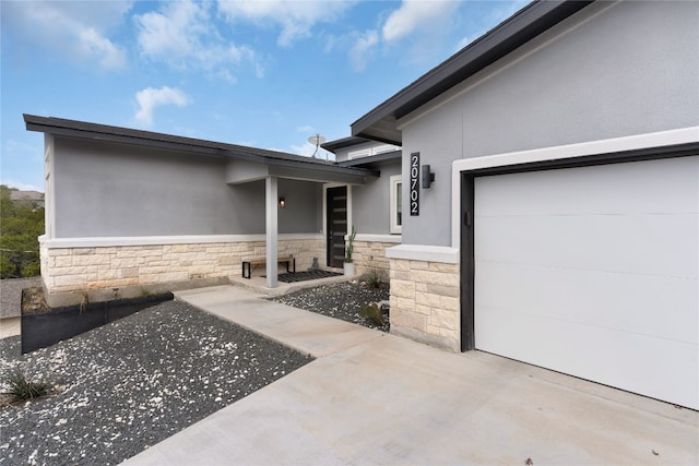 entrance to property with a garage, stone siding, and stucco siding