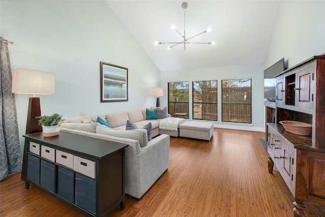 living room with high vaulted ceiling, an inviting chandelier, and light hardwood / wood-style flooring