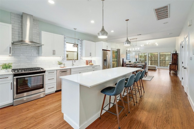 kitchen featuring stainless steel appliances, a kitchen island, white cabinets, and wall chimney exhaust hood