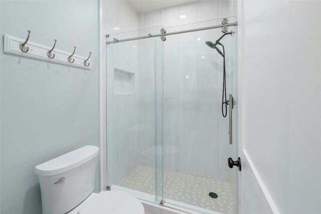 bathroom featuring a shower with door and toilet