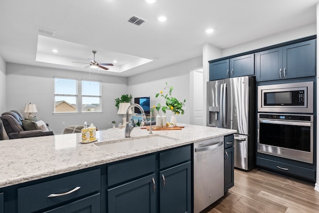 kitchen featuring sink, a raised ceiling, hardwood / wood-style flooring, stainless steel appliances, and light stone countertops